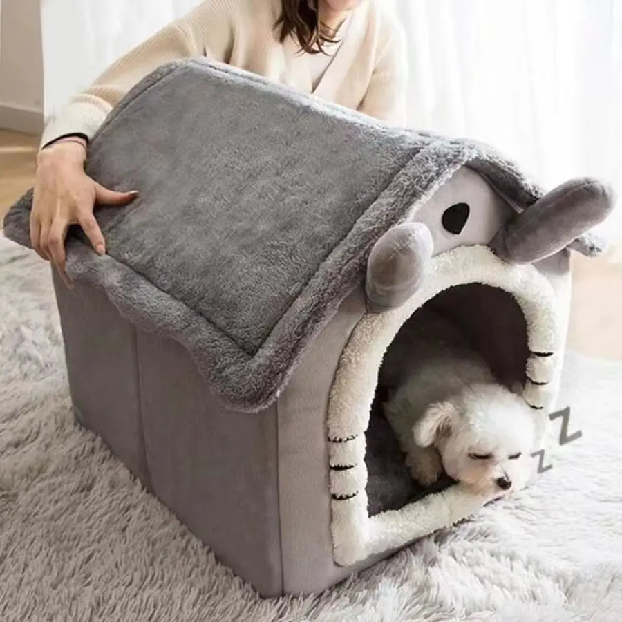 Small white dog resting inside a grey house-style pet bed with a soft roof